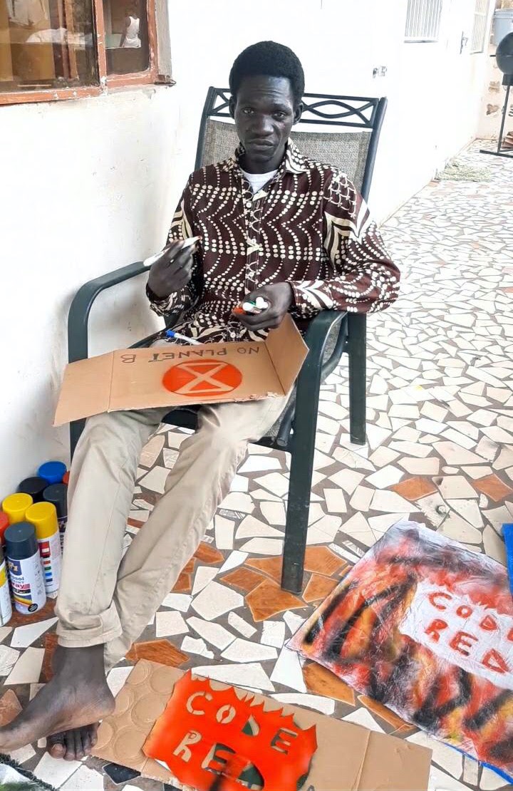 Babu sits outside making signs of protest using carrdboard stencils and coloured pens